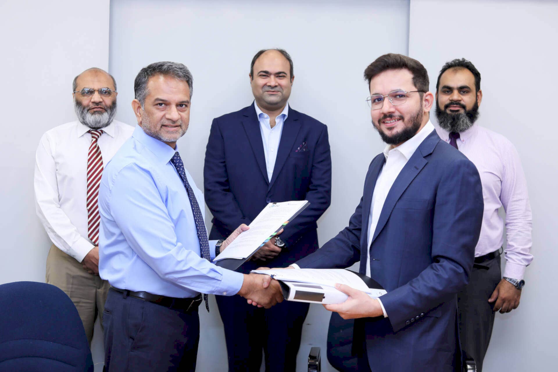 The image captures a formal signing ceremony between two individuals at the forefront—Sumair Sayani, Prima Consulting’s Director of AI and Tech, and Baber Mirza, Atlas Insurance’s Chief Executive Officer. Behind them stand three other people: Ibrahim Ahmed Zahidie (Director of Financial and Accounting Advisory), and Omer Yousuf (Vice President). The background features a corporate logo reading “Delta,” symbolizing the partnership.