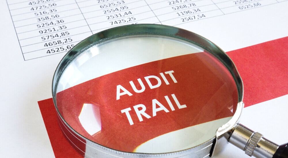 The image shows a magnifying glass highlighting the words "Audit Trail" on a document, symbolizing detailed examination and tracking. For Prima Consulting's Delta IFRS 17 Software, it emphasizes the comprehensive audit trail feature that logs every action within the system. This includes tracking who initiates provisions, approves them, and manages data uploads and approvals. The transparency provided by this audit trail upholds accountability and ensures strict adherence to IFRS 17 regulations.