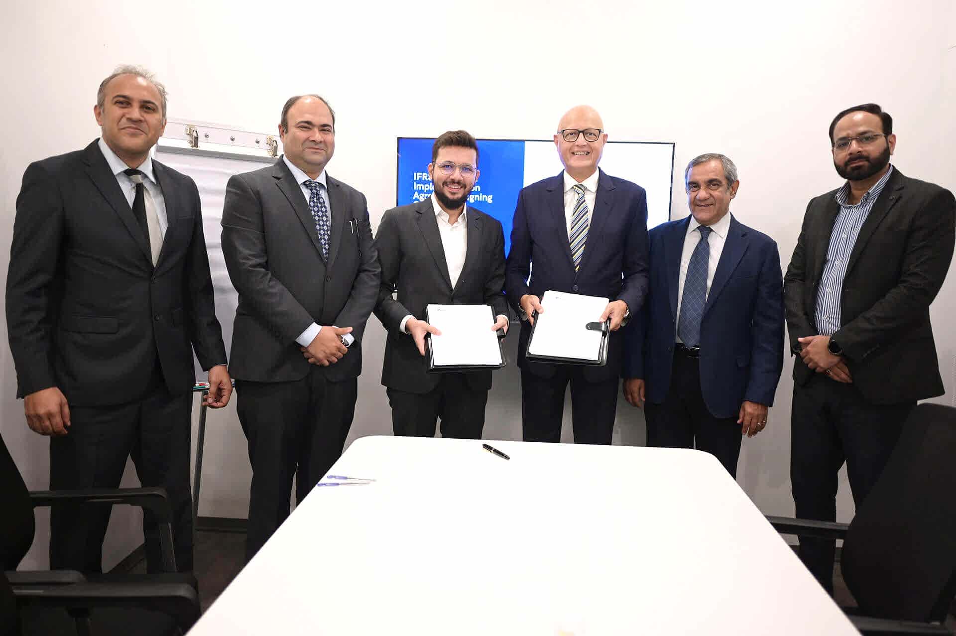 Six executives in business suits stand in an office setting with two central figures (Sumair Sayani, Director of AI and Tech at Prima Consulting and Syed Ather Abbas, CEO of Habib Insurance) holding documents, symbolizing a formal business agreement. A whiteboard and digital screen are visible behind them.