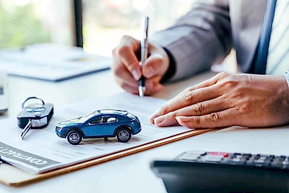 A close-up image of a person’s hands, one holding a pen, with a small blue car model on a desk, keys beside it, and documents underneath. This setting suggests the theme of lease accounting and compliance in line with IFRS 16 standards.