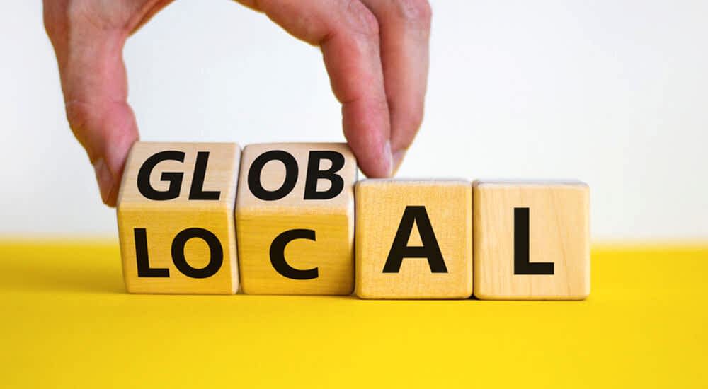 A hand flipping one wooden block in a series, changing the word ‘LOCAL’ to ‘GLOBAL.’ The blocks are set against a bright yellow background, symbolizing the adaptability and global reach of a system initially tailored for local markets in the Middle East and Pakistan. This represents the system’s compliance with regional labor laws while highlighting its capability to expand and operate globally.